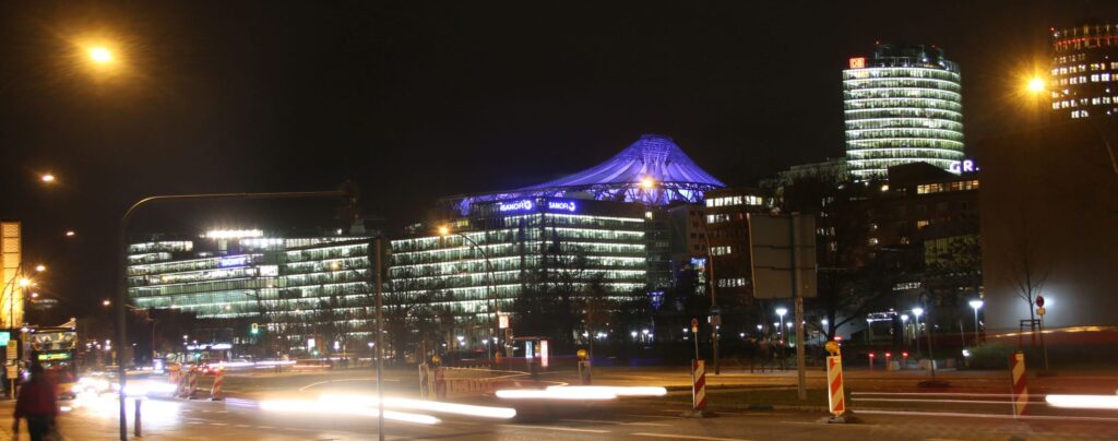 Sony-Center Berlin bei Nacht mit Straßenverkehr im Vordergrund und fahrenden Autos.